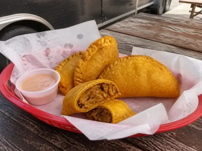 Golden fried empanadas with a dipping sauce in a red basket